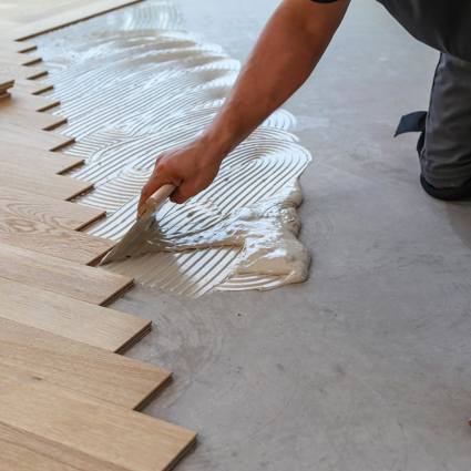 Person applying adhesive to floor to lay wooden flooring