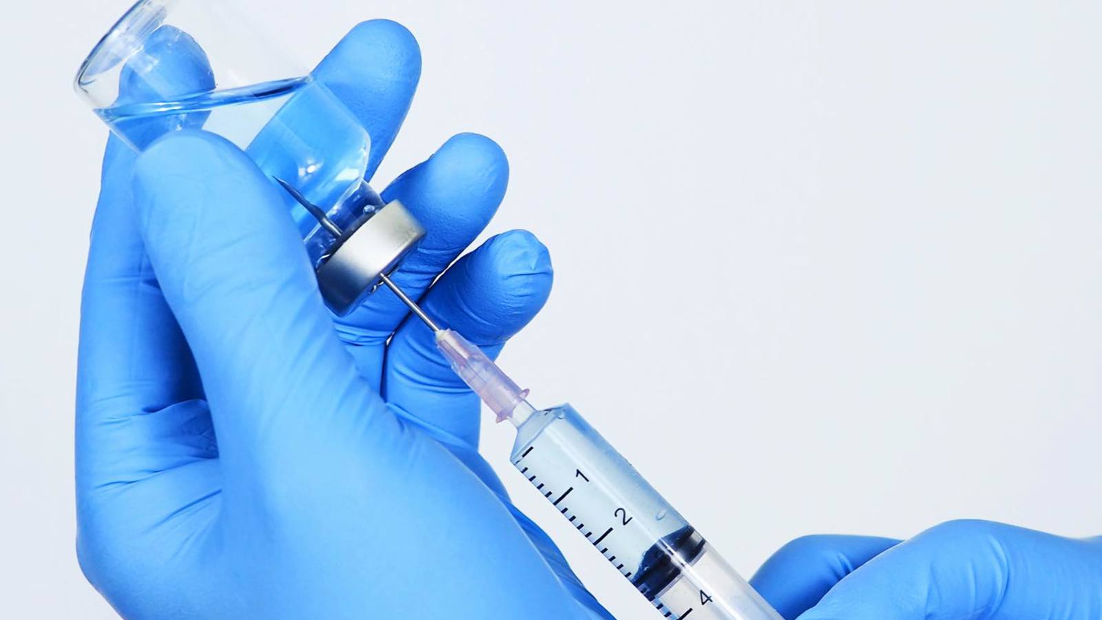 Person wearing gloves filling a syringe
