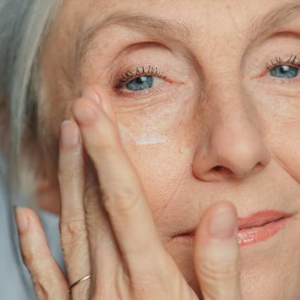 Senior person applying cream to face